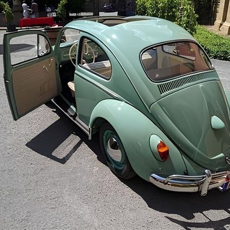 Ein türkiser VW Käfer steht auf einer Straße, Heckansicht.