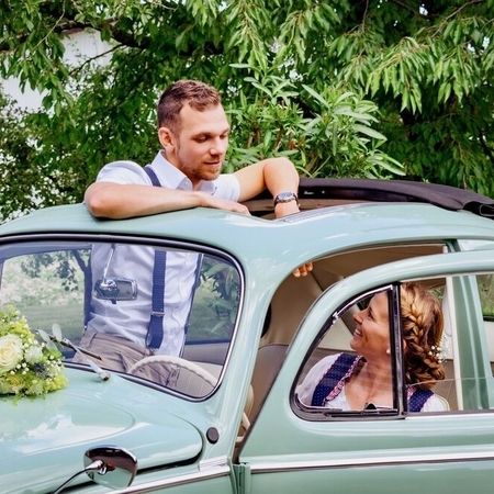 Ein Brautpaar sitzt in einem türkisen VW Käfer und erlebt gemeinsam einen Moment der Entspannung und Freude.