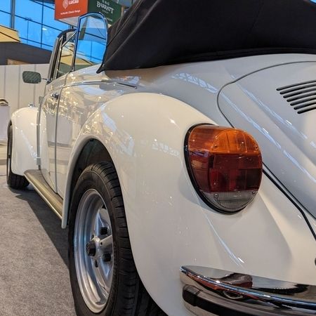 Der VW Käfer Cabrio 1303 in Hellelfenbein in einer Halle, Heckansicht.