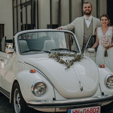 Der VW Käfer Cabrio 1303 steht auf einer Straße und daneben ein Brautpaar.