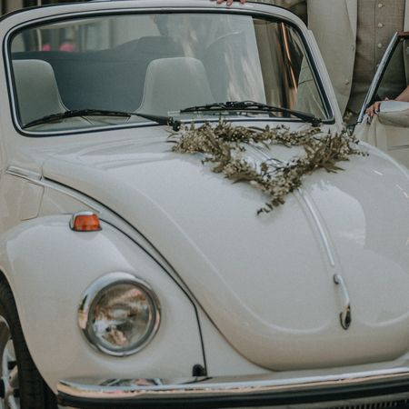 Der VW Käfer Cabrio 1303 steht auf einer Straße und daneben ein Brautpaar.